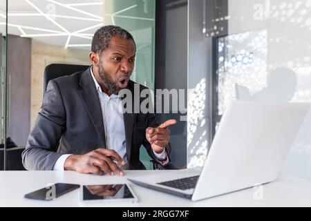 Wütender, nervöser Geschäftsmann, der per Fernzugriff per Videoanruf mit einem Laptop telefoniert, erfahrener erfahrener erfahrener erfahrener erfahrener, reifer Chef, der schreit und sich am Arbeitsplatz im Büro streitet. Stockfoto