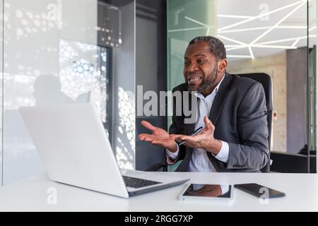 Wütender, nervöser Geschäftsmann, der per Fernzugriff per Videoanruf mit einem Laptop telefoniert, erfahrener erfahrener erfahrener erfahrener erfahrener, reifer Chef, der schreit und sich am Arbeitsplatz im Büro streitet. Stockfoto