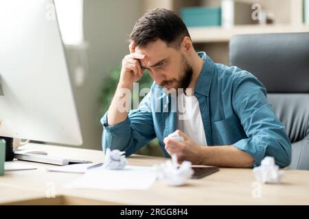 Verärgerter Gestresster Geschäftsmann, Der Papier Zerbröselt Hat, Während Er Am Schreibtisch Im Büro Saß Stockfoto