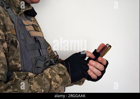 Ukrainischer Soldat in Uniform mit Smartphone. Ein Banner der ukrainischen Flagge auf einer Tarnuniform eines Soldaten. Ukrainische Flagge auf Chevron in BL Stockfoto