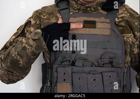 Ukrainischer Soldat in militärischer Pixel-Unform und kugelsicherer Weste mit Banner der ukrainischen Flagge und Finger in schwarzem Handschuh. Stockfoto