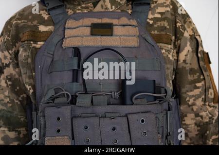 Ukrainischer Soldat in grauer kugelsicherer Jacke mit Banner der ukrainischen Flagge und Powerbank. Stockfoto