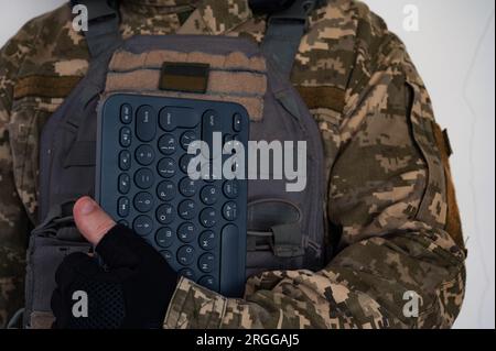 Ukrainischer Soldat in grauer kugelsicherer Jacke mit Symbol der ukrainischen Flagge und Tastatur in schwarzem Handschuh. Stockfoto