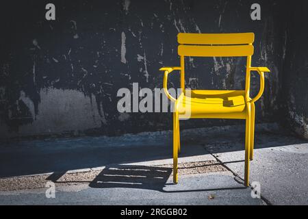 Gelber moderner Gartenstuhl vor alten Betonwänden, hoher Kontrast von Sonne und Schatten, modernes Stadtkonzept Stockfoto