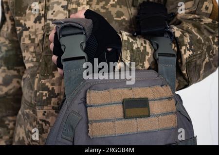 Der Soldat hält eine graue kugelsichere Jacke mit einem Banner der ukrainischen Flagge im Arm in schwarzem Handschuh. Stockfoto