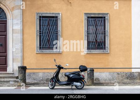 Schwarzer Roller auf dem Bürgersteig vor einem historischen italienischen Haus mit gelb verputzten Wänden, Steinsäulen und großer Holztür Stockfoto