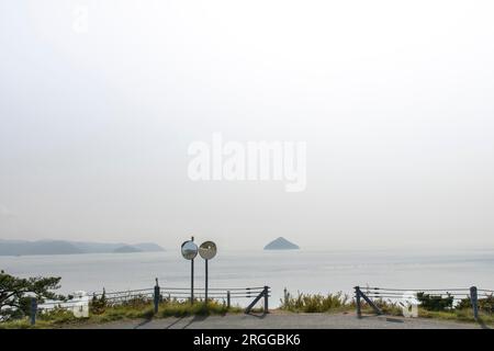 Zwei konvexe Verkehrsspiegel in einer Straßenecke mit Panoramablick auf das japanische Seto-Binnenmeer in der Nähe der Insel Naoshima mit Nebel und Misstrauen Stockfoto