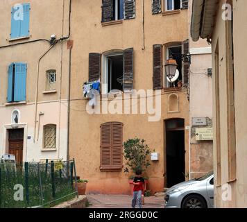 Ein Junge läuft glücklich in die Nähe seines Hauses; seine Schwester schaut ihm aus einem verschlossenen Fenster zu. Altstadt von Fréjus, provenzalisches Dorf im Var, SE Frankreich Stockfoto