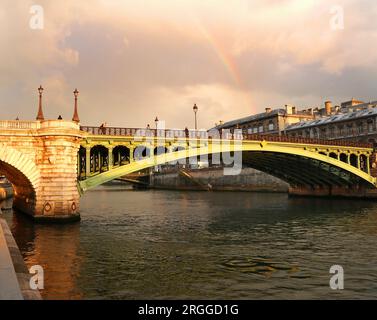 Das grüne Metall der Pont Notre Dame, die die seine in Paris überquert, leuchtet nach starkem Regen im frühen Abendlicht unter einem schwachen Regenbogen Stockfoto