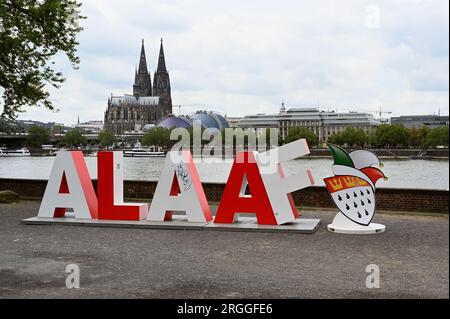 Köln, Deutschland. 09. Aug. 2023. Die 2 m lange Schriftgröße Alaaf steht am Rheinufer vor dem Rhein und dem Kölner Dom als Geschenk des Kölner Karnevalskomitees zum 200. Jahrestag des Karnevals. Alaaf ist weltberühmt als traditionelles Kölner Ausrufezeichen und ein echtes Markenzeichen der rhenischen Lebensfreude. Kredit: Horst Galuschka/dpa/Alamy Live News Stockfoto