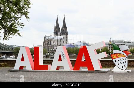 Köln, Deutschland. 09. Aug. 2023. Die 2 m lange Schriftgröße Alaaf steht am Rheinufer vor dem Rhein und dem Kölner Dom als Geschenk des Kölner Karnevalskomitees zum 200. Jahrestag des Karnevals. Alaaf ist weltberühmt als traditionelles Kölner Ausrufezeichen und ein echtes Markenzeichen der rhenischen Lebensfreude. Kredit: Horst Galuschka/dpa/Alamy Live News Stockfoto