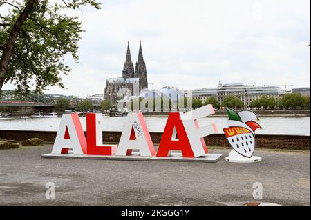 Köln, Deutschland. 09. Aug. 2023. Die 2 m lange Schriftgröße Alaaf steht am Rheinufer vor dem Rhein und dem Kölner Dom als Geschenk des Kölner Karnevalskomitees zum 200. Jahrestag des Karnevals. Alaaf ist weltberühmt als traditionelles Kölner Ausrufezeichen und ein echtes Markenzeichen der rhenischen Lebensfreude. Kredit: Horst Galuschka/dpa/Alamy Live News Stockfoto