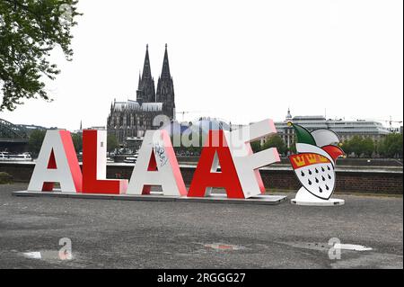 Köln, Deutschland. 09. Aug. 2023. Die 2 m lange Schriftgröße Alaaf steht am Rheinufer vor dem Rhein und dem Kölner Dom als Geschenk des Kölner Karnevalskomitees zum 200. Jahrestag des Karnevals. Alaaf ist weltberühmt als traditionelles Kölner Ausrufezeichen und ein echtes Markenzeichen der rhenischen Lebensfreude. Kredit: Horst Galuschka/dpa/Alamy Live News Stockfoto