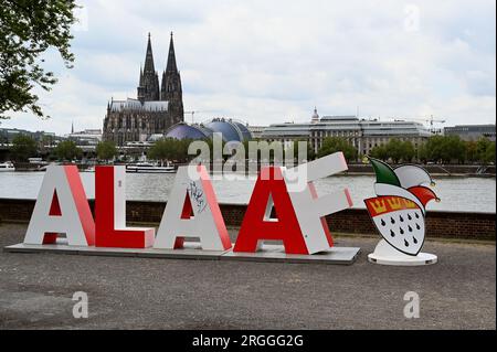 Köln, Deutschland. 09. Aug. 2023. Die 2 m lange Schriftgröße Alaaf steht am Rheinufer vor dem Rhein und dem Kölner Dom als Geschenk des Kölner Karnevalskomitees zum 200. Jahrestag des Karnevals. Alaaf ist weltberühmt als traditionelles Kölner Ausrufezeichen und ein echtes Markenzeichen der rhenischen Lebensfreude. Kredit: Horst Galuschka/dpa/Alamy Live News Stockfoto