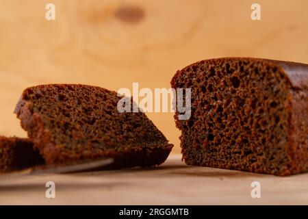 Dunkles Brotlaaf und seine geschnittenen Gegenstücke auf hellem beigefarbenem Holzhintergrund Stockfoto