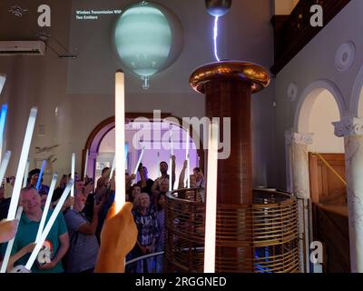 Menschen, die ein Experiment mit Stangen in der Hand genießen, während ein Blitz im Nikola Tesla Museum in Belgrad, Serbien, erscheint. August 2023. Stockfoto