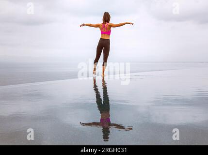Eine Frau, die mit ausgestreckten Armen am Meer steht Stockfoto