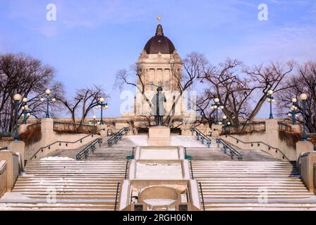 Blick auf den Winter vom Ufer des Assiniboine River auf das Manitoba Legislature Gebäude mit Louis Riel Skulptur in Winnipeg, Manitoba, Kanada. Erstellt in Stockfoto