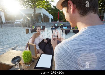 Junge Menschen machen Fotos der jungen Frau am Strand Stockfoto