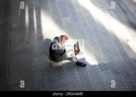 Blick von oben auf einen Geschäftsmann, der ein Laptop auf der Treppe benutzt Stockfoto