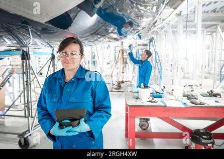Frau, die ein digitales Tablet im Flugzeug im Hangar hält Stockfoto