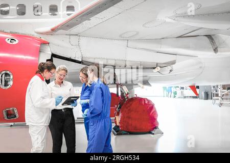 Arbeiterinnen, die ein digitales Tablet im Flugzeughangar benutzen Stockfoto