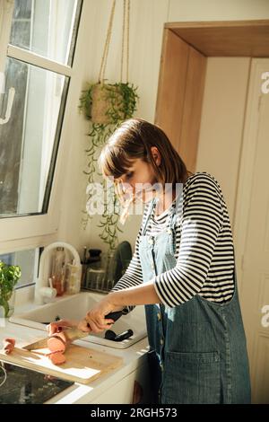 Junge Frau, die Süßkartoffeln schneidet Stockfoto