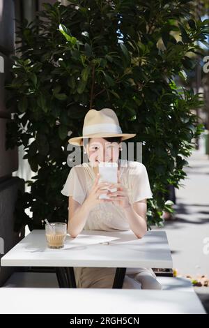 Eine Frau mit Strohhut am Tisch, die ein Smartphone benutzt Stockfoto