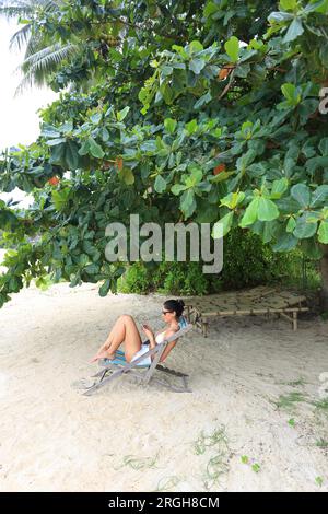 Junge Frau sitzt auf der Liege am Strand. Stockfoto