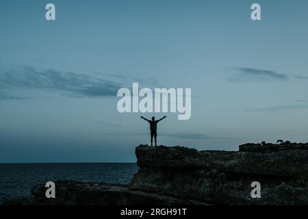 Die Silhouette eines jungen Mannes mit Arme auf Felsen bei Calo des Moro ausgestreckt auf Mallorca Stockfoto
