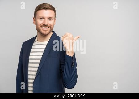 Glücklicher, freundlicher Mann in der Jacke, der Daumenfinger auf grauem Hintergrund zeigt. Stockfoto