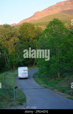 Wohnmobil fährt Bergstraße mit grünem Wald und hohen Bergen mit blauem Himmel vertikal hinauf Stockfoto