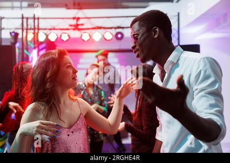 Mann und Frau, verschiedene Freunde, die auf einer Disco-Party tanzen und sich unterhalten. Ein junges, multiethnisches Paar, das in Clubs schläft und Spaß auf Tanzfläche in der Diskothek im Club hat Stockfoto