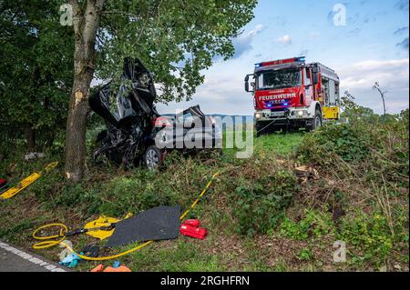 Halver, Deutschland. 09. Aug. 2023. Ein Feuerwehrauto steht neben einem schwer beschädigten Auto. Ein 20-jähriger Fahrer wurde bei einem Unfall in seinem Auto in Halver (Märkischer Kreis) gefangen und starb. Laut der Polizei in Iserlohn verließ der junge Mann aus Schalksmühle am Mittwochabend die Straße aus noch unbekannten Gründen und kollidierte mit einem Baum. Kredit: Markus Klümper/dpa - ACHTUNG: Das Nummernschild wurde aus rechtlichen Gründen verpixelt/dpa/Alamy Live News Stockfoto