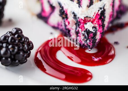 Nahaufnahme einer Scheibe Blackberry Zebra Cake Dessert mit Blackberry Sauce auf einem Weißteller Stockfoto