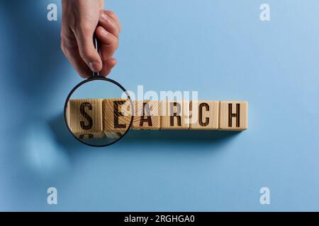Lupe und Suchbegriff auf Würfel auf Holzhintergrund geschrieben Stockfoto