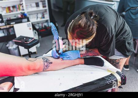 Volle Konzentration auf die Arbeit. Rohe und echte Tätowierung, fotografiert in einem Tattoo-Studio-Interieur. Tätowierungskünstlerin bei der Arbeit. Hochwertiges Foto Stockfoto