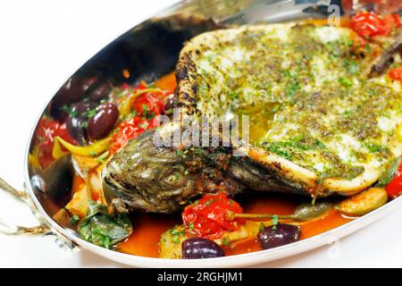 mediterraner gebackener Seebarschfisch mit Tomaten, Kapern, Artischocken, Olivensauce Stockfoto