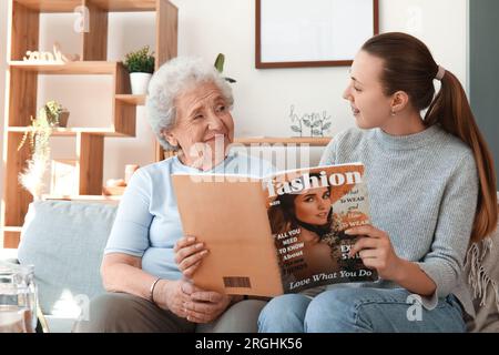 Seniorin mit ihrer Enkelin, die zu Hause Zeitschriften liest Stockfoto