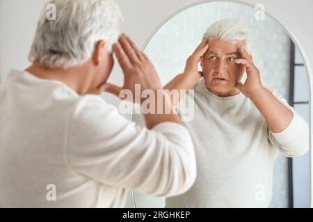 Schockierter Senior-Mann, der zu Hause in den Spiegel schaut Stockfoto