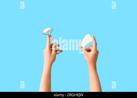 Frau mit Gesichtsmassagewalze und Gua-Sha auf blauem Hintergrund Stockfoto