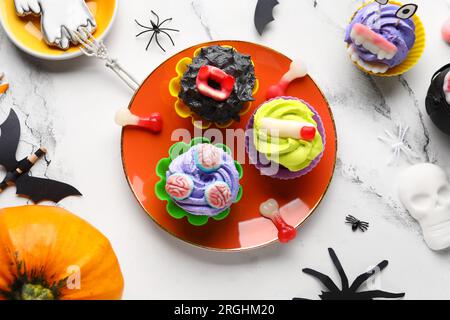 Zusammensetzung mit köstlichen Halloween-Cupcakes, Süßigkeiten und Dekor auf hellem Hintergrund Stockfoto