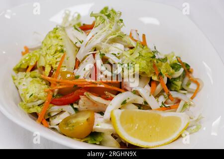 Meeresfrüchtesalat mit Tintenfisch, Garnelen, Garnelen, Tintenfisch, Salat und Tomaten in einer weißen Schüssel Stockfoto