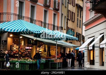 Farbenfrohe Stadthäuser und ein wöchentlicher Bauernmarkt in der Fußgängerzone der Altstadt von Lugano, Schweiz. Stockfoto