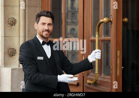 Butler in elegantem Anzug und weiße Handschuhe öffnen die hölzerne Hoteltür Stockfoto