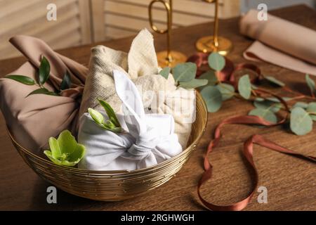 Furoshiki-Technik. Geschenke verpackt in verschiedenen Stoffen und Blumen auf Holztisch, Nahaufnahme. Platz für Text Stockfoto