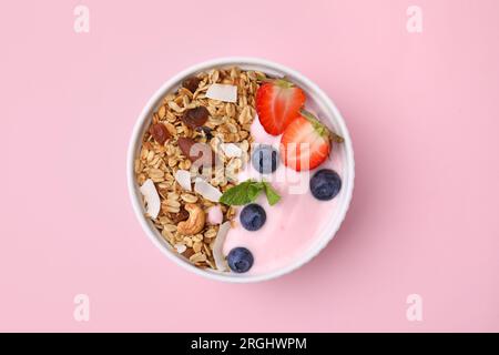 Leckeres Müsli, Joghurt und frische Beeren in der Schüssel auf pinkfarbenem Hintergrund, Draufsicht. Gesundes Frühstück Stockfoto