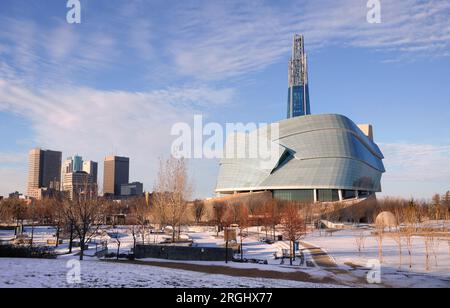 Sonniger Sonnenuntergang an einem Wintertag in Winnipeg im Stadtzentrum. Winterblick auf das Canadian Museum for Human Rights im Vordergrund und Hochhäuser von Winnipeg Stockfoto