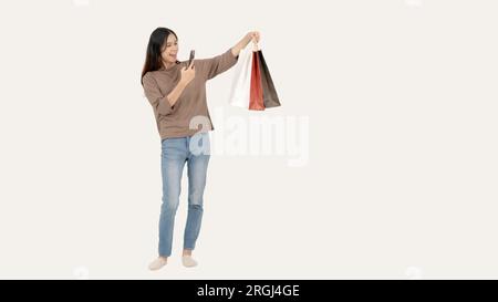 Eine fröhliche Asiatin fotografiert ihre Einkaufstüten, während sie vor einem isolierten weißen Hintergrund steht. Shopping und Lifestyle c Stockfoto