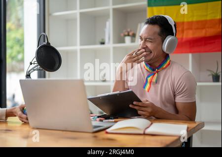 Ein attraktiver und fröhlicher Radiosender für asiatische Homosexuelle lacht und unterhält sich gerne, während er mit seinem Gast einen Audio-Podcast aufnimmt Stockfoto